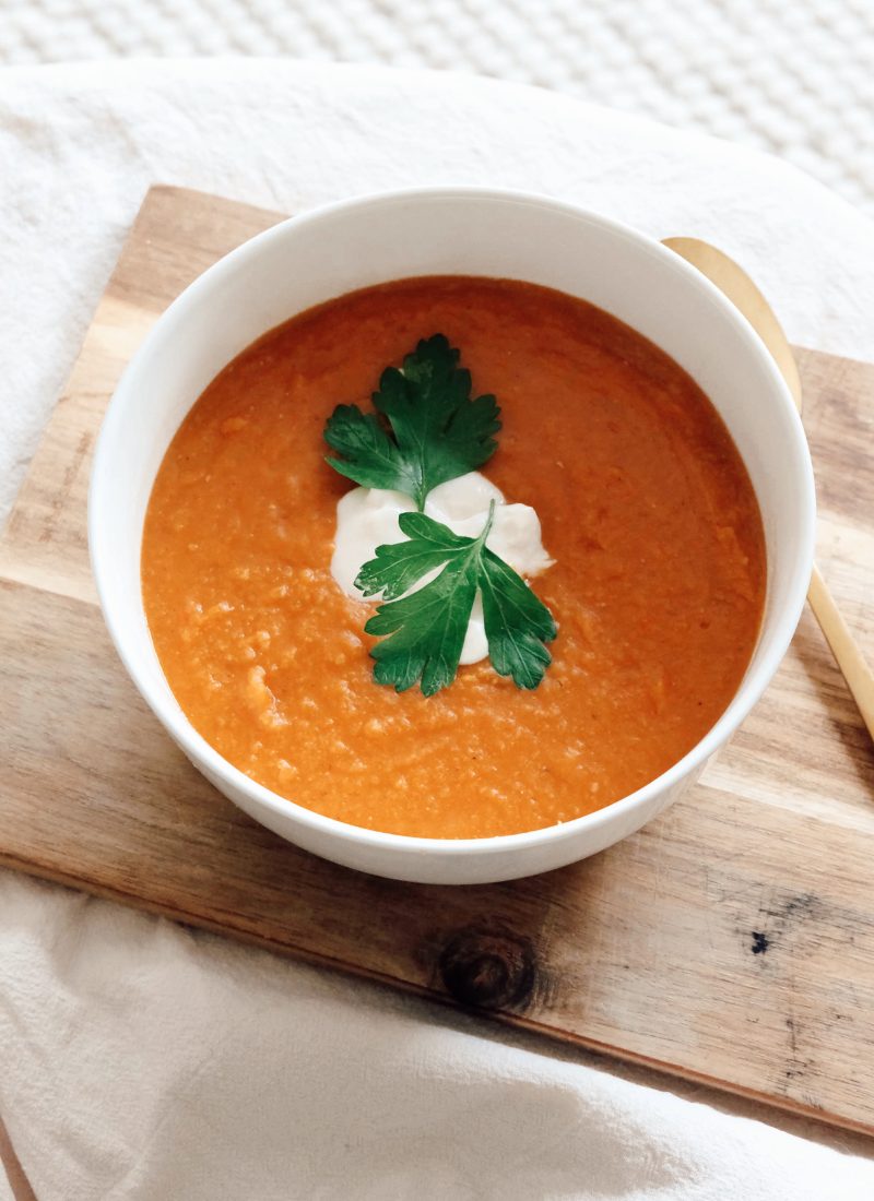 Red lentil soup garnished with parsley and yoghurt in a ceramic bowl with a golden spoon